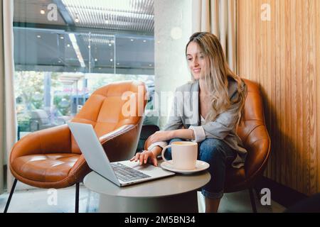 Peaceful millennial business woman using computer, with mug of coffee in modern workplace.  Stock Photo