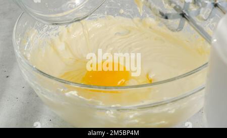 Cream cheese, eggs, and sugar in a bowl. Cheesecake recipe, mixing ingredients in a glass bowl, close-up view Stock Photo