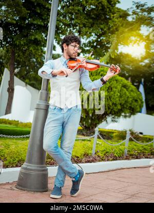 Man playing violin in the street. Portrait of man playing violin in the street. Jacket artist playing violin outdoors, Image of a person playing Stock Photo