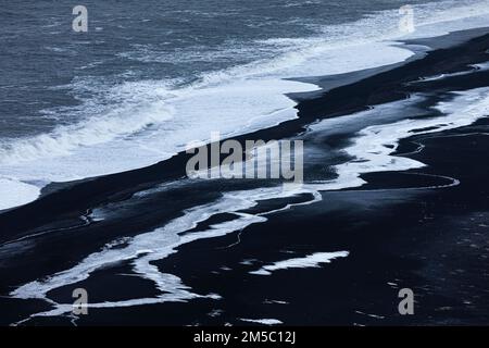 Foamy white waves and icy surfaces on the black pebble beach Skogarsandur, near Dyrholaey, Sudurland, Iceland Stock Photo