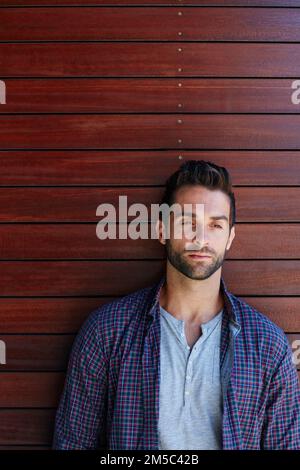 Letting his mind wander. a handsome man standing against a wooden wall. Stock Photo