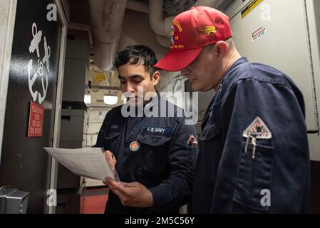 220224-N-XB010-1001 PACIFIC OCEAN (Feb. 24, 2022) Damage Controlman 3rd Class Emerson Ovando, from San Fernando Valley, Calif., left, explains to Damage Controlman 1st Class Gary Sells, Damage Control Training Team instructor aboard USS New Orleans (LPD 18), the steps that he took to appropriately secure a material condition of readiness zone of the ship during a general quarters drill. New Orleans, part of the America Amphibious Ready Group, is operating in the U.S. 7th Fleet area of responsibility to enhance interoperability with allies and partners and serve as a ready response force to def Stock Photo