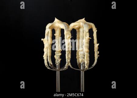 Mixer whisks with yellow mayonnaise, isolated on black background, soft focus close up Stock Photo