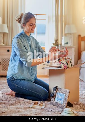 Taking a trip down memory lane. a young woman unpacking a box at home. Stock Photo
