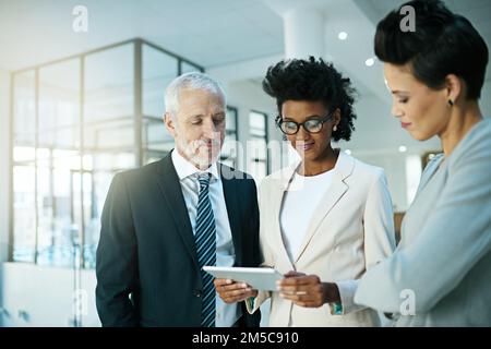 Updating the team as to where they are. a business team using a digital tablet while having an informal meeting. Stock Photo