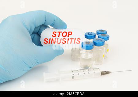Medical concept. In the man's hand is a piece of paper with the inscription - STOP SINUSITIS, next to it lies a syringe and injection jars. Stock Photo