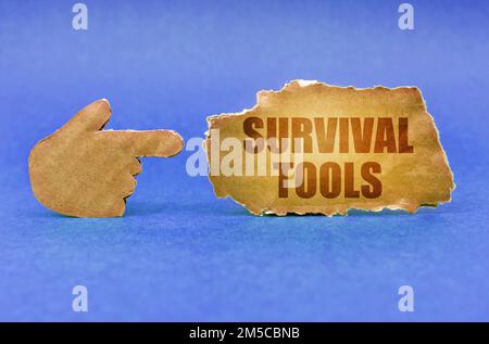 Business concept. On a blue surface, a cardboard hand points to a sign with the inscription - Survival Tools Stock Photo