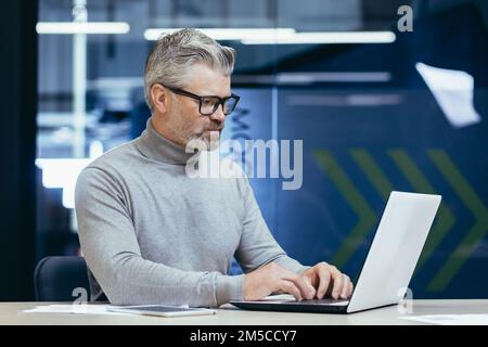Serious thinking businessman inside office at work with laptop, senior gray haired man working sitting at desk. Stock Photo