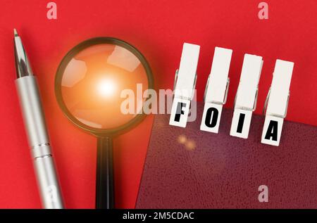 Business concept. On the red surface there is a magnifying glass, a notepad and clothespins with the inscription - FOIA Stock Photo