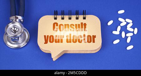 Medical concept. On the blue surface of the tablet, a stethoscope and a notepad with the inscription - Consult your doctor Stock Photo