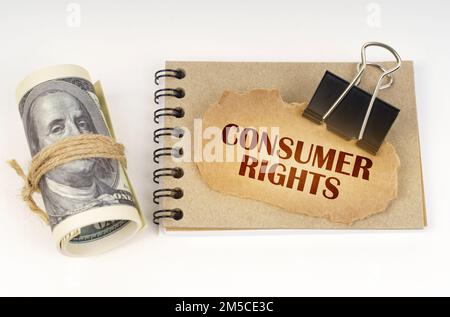 Business and finance concept. On a white surface are twisted dollars, a notebook and a cardboard sign with the inscription - CONSUMER RIGHTS Stock Photo