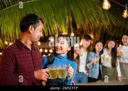 Happy young Asian couple having a party with friends while drinking beer. Stock Photo
