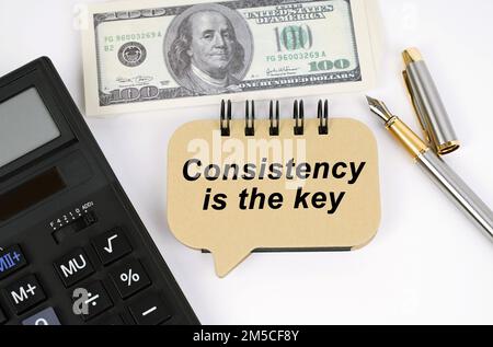 Business concept. On a white surface, a calculator, dollars, a pen and a sign with the inscription - Consistency Is The Key Stock Photo