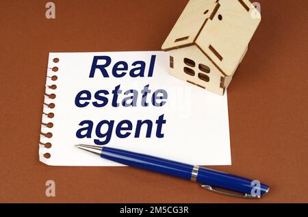 Business concept. On a brown surface is a house, a pen and a notepad with the inscription - Real Estate Agent Stock Photo