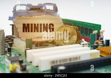 Crypto - business concept. On the motherboard lies a bitcoin coin and a cardboard sign with the inscription - Mining Stock Photo
