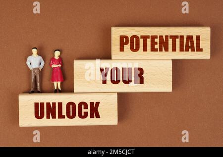 Business concept. On a brown surface, wooden blocks with the inscription - UNLOCK YOUR POTENTIAL. There are figures of people on the blocks. Stock Photo