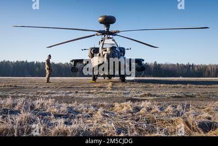 A U.S. Army Soldier assigned to 1-3rd Attack Battalion, 12th Combat Aviation Brigade gazes at an AH-64D Apache Longbow helicopter belonging to 1-3 AB, 12 CAB, rests under the sun prior to a air assault exercise conducted by the United States, Lithuania, and the United Kingdom, at Kazlu Ruda, Lithuania, March 1, 2022. Saber Strike and exercises like it show that the U.S. and European forces can simultaneously support ongoing operations and regularly scheduled training without degradation in supporting NATO allies and partners. Stock Photo