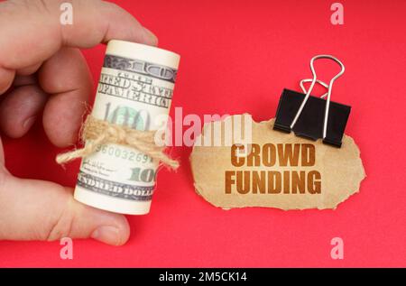 Business concept. The man has dollars in his hands, on a red surface there is a cardboard sign with the inscription - CROWD FUNDING Stock Photo