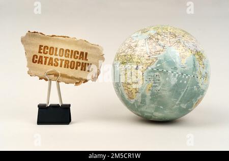 Ecological concept. Near the globe there is a clip with a cardboard plate on which it is written - Ecological catastrophy Stock Photo