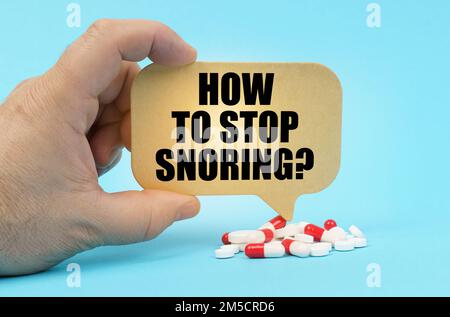Medical concept. On a blue surface are pills in a persons hand, a sign with the inscription - HOW TO STOP SNORING Stock Photo