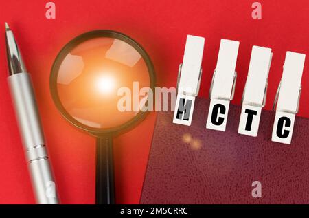 Business concept. On the red surface there is a magnifying glass, a notepad and clothespins with the inscription - HCTC Stock Photo