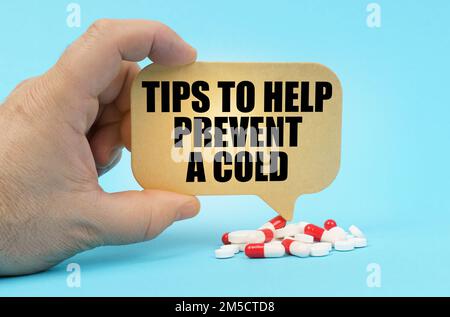 Medical concept. On a blue surface are pills in a persons hand, a sign with the inscription - Tips to help prevent a cold Stock Photo