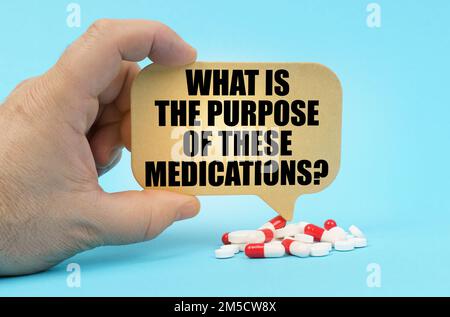 Medical concept. On a blue surface are pills in a persons hand, a sign with the inscription - What is the purpose of these medications Stock Photo