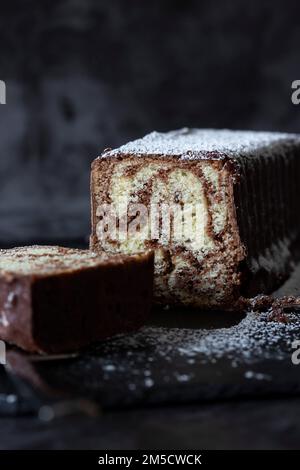 Homemade chocolate marble cake on a slate cutting board covered with icing sugar. Piece cut with a cake slicer Stock Photo