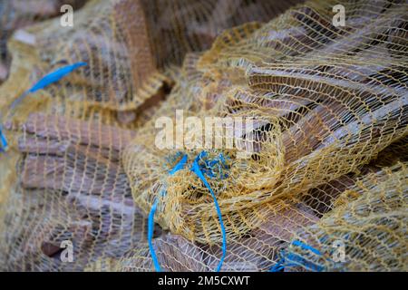Small pieces of firewood packed in a yellow nylon net, offered for sale in a shop. Easily combustible small sticks or wood used for starting a fire Stock Photo