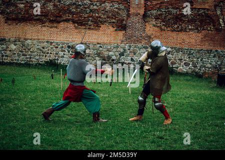 Sword fight of two knights in helmets and chain mail armor in scenery of medieval castle Stock Photo