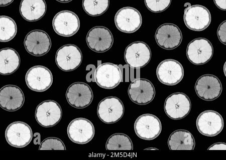 Pattern made of backlit citrus fruits slices on black background Stock Photo