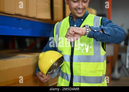 Smiling storehouse worker looking at wristwatch to managing time during working in retail warehouse Stock Photo