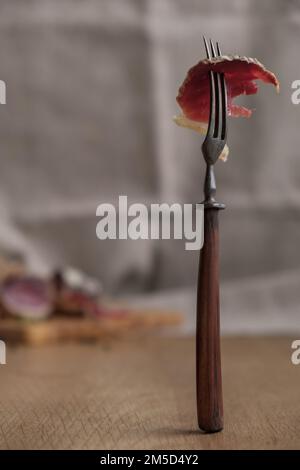 Close-up piece of jamon on fork, light appetizer, homemade food, selective focus Stock Photo