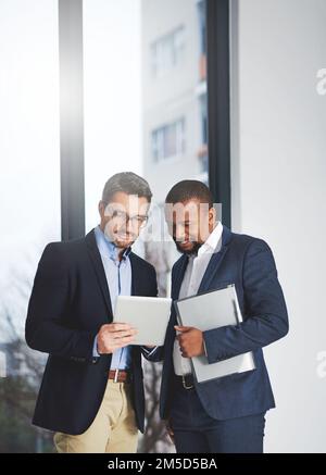 Increasing productivity with business savvy apps. two businessmen using a digital tablet together at work. Stock Photo