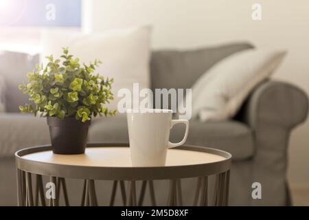 cup of hot tea. white mug on table near cozy gray sofa. pillows and blanket. Home relax Lifestyle Stock Photo