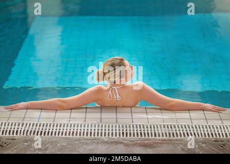Calming waters to clear the mind. Rearview shot of a young woman relaxing in the pool at a spa. Stock Photo