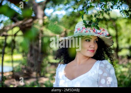 A portrait of pretty young woman wearing white dress and summer hat while posing in the park Stock Photo