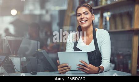 Reach more coffee lovers on the net. a young woman using a digital tablet in the store that she works at. Stock Photo