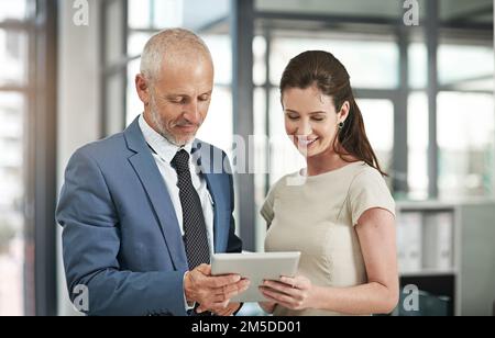 Figuring it out between the two of them. two businesspeople working together on a digital tablet in a modern office. Stock Photo