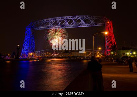 Fireworks behind an aerial lift bridge lit up in red, white, and blue. Stock Photo
