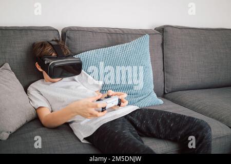 Boy having fun playing simulation games, using virtual reality headset and controller. Children and modern technology concept. Stock Photo