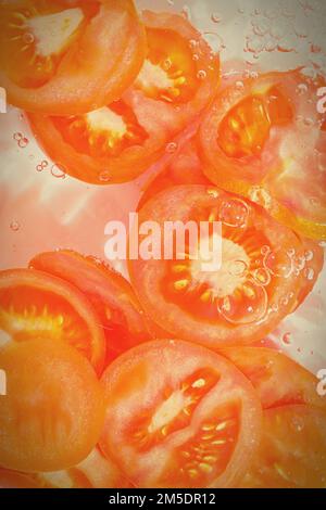 Close-up fresh slices of tomato on white background. Slices of tomato in sparkling water on white background, close-up. Vertical image Stock Photo
