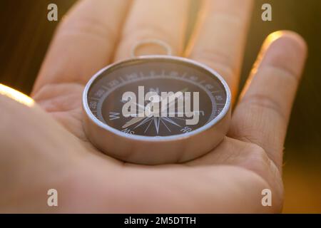 Compass in hand on natural pine forest background. hand holding compass in forest landscape. Young traveler searching direction with compass in summer Stock Photo