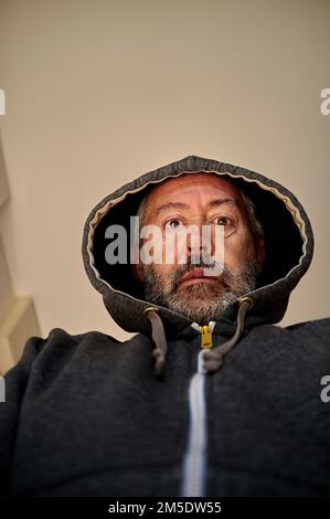 worried middle aged man in hooded jacket, looking down Stock Photo