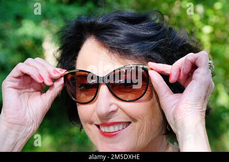 Attractive mature female holding a pair of sunglasses - John Gollop Stock Photo