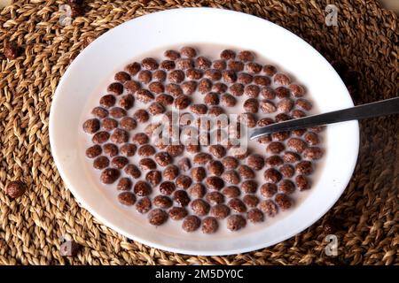photo chocolate balls floating in milk in a plate with a spoon Stock Photo