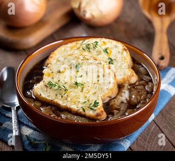 Closeup of french onion soup with toasted cheese baguette garnished with thyme on a rustic wooden table background Stock Photo