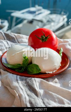 White soft italian mozzarella bufala cheese in balls with red tomato and basil served outdoor Stock Photo