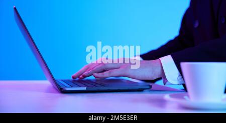 Business woman working, typing on laptop over blue background in neon lights. Working process. Stock Photo