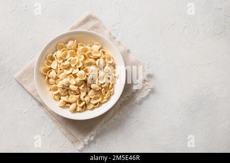 Fresh raw orecchiette pasta made from whole wheat flour in bowl on white background. Copy space. Top view. Stock Photo